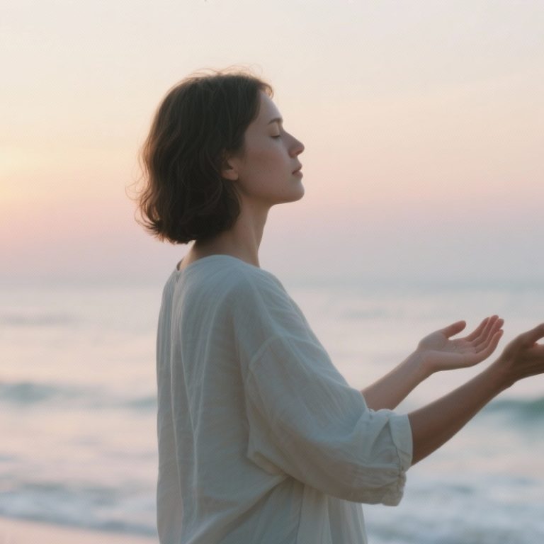 Person standing by the ocean at sunrise with open hands, symbolizing letting go, calm, and emotional healing.